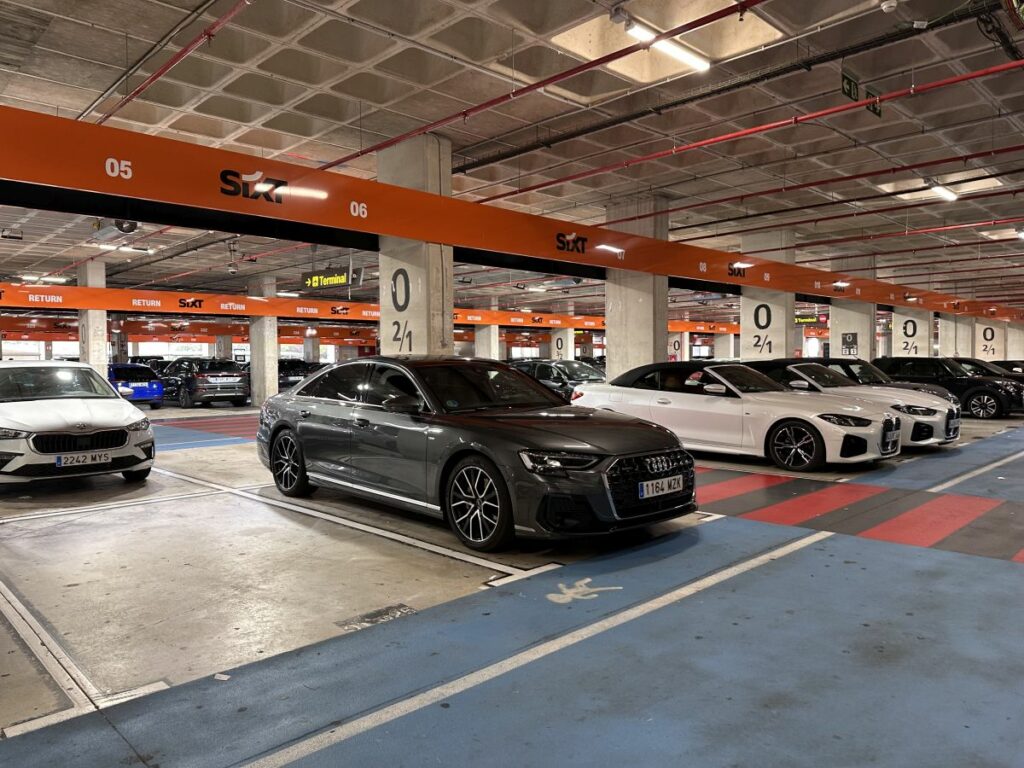 Mehrere geparkte Autos, darunter ein grauer Audi und weiße BMWs, im Sixt Mietwagen-Parkhaus mit markierten Stellplätzen