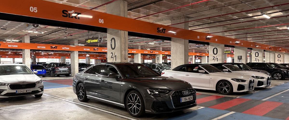 Parkhaus einer Sixt-Autovermietung mit mehreren hochwertigen Fahrzeugen, darunter ein grauer Audi A8 und weiße BMW-Modelle, die in markierten Stellplätzen bereitstehen.