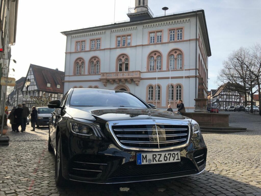 Schwarzer Mercedes-Benz S-Klasse, Frontansicht mit Kühlergrill und Stern-Emblem, geparkt auf Kopfsteinpflaster vor historischem Rathaus